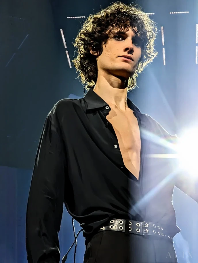 Close-up of sombr in a black shirt with a bright stage light behind him.