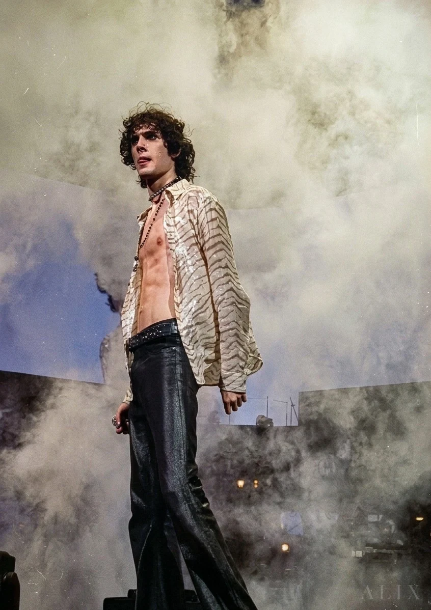 sombr standing on stage in a patterned jacket surrounded by drifting smoke.