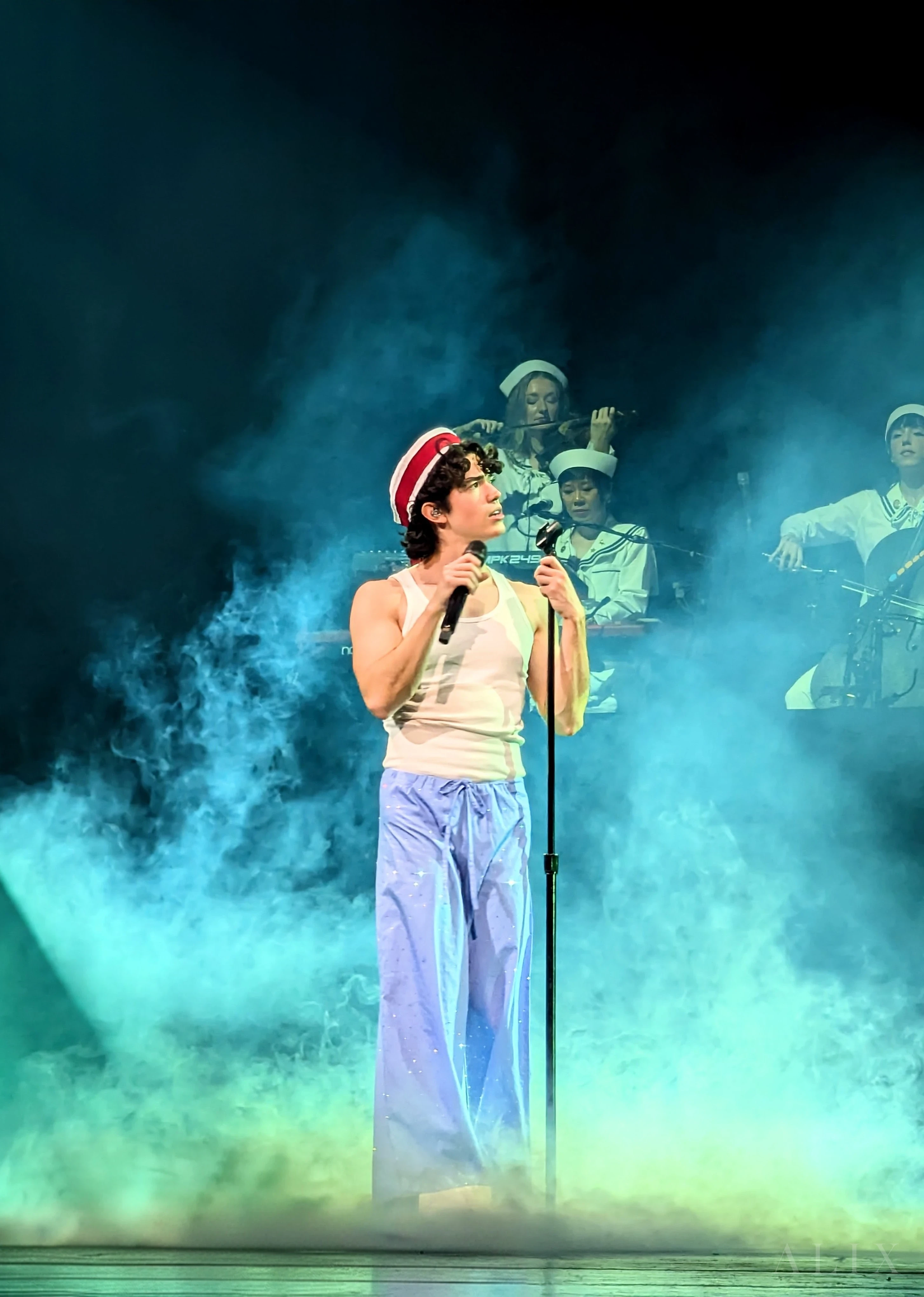 Conan Gray stands at the microphone surrounded by blue-green stage smoke.