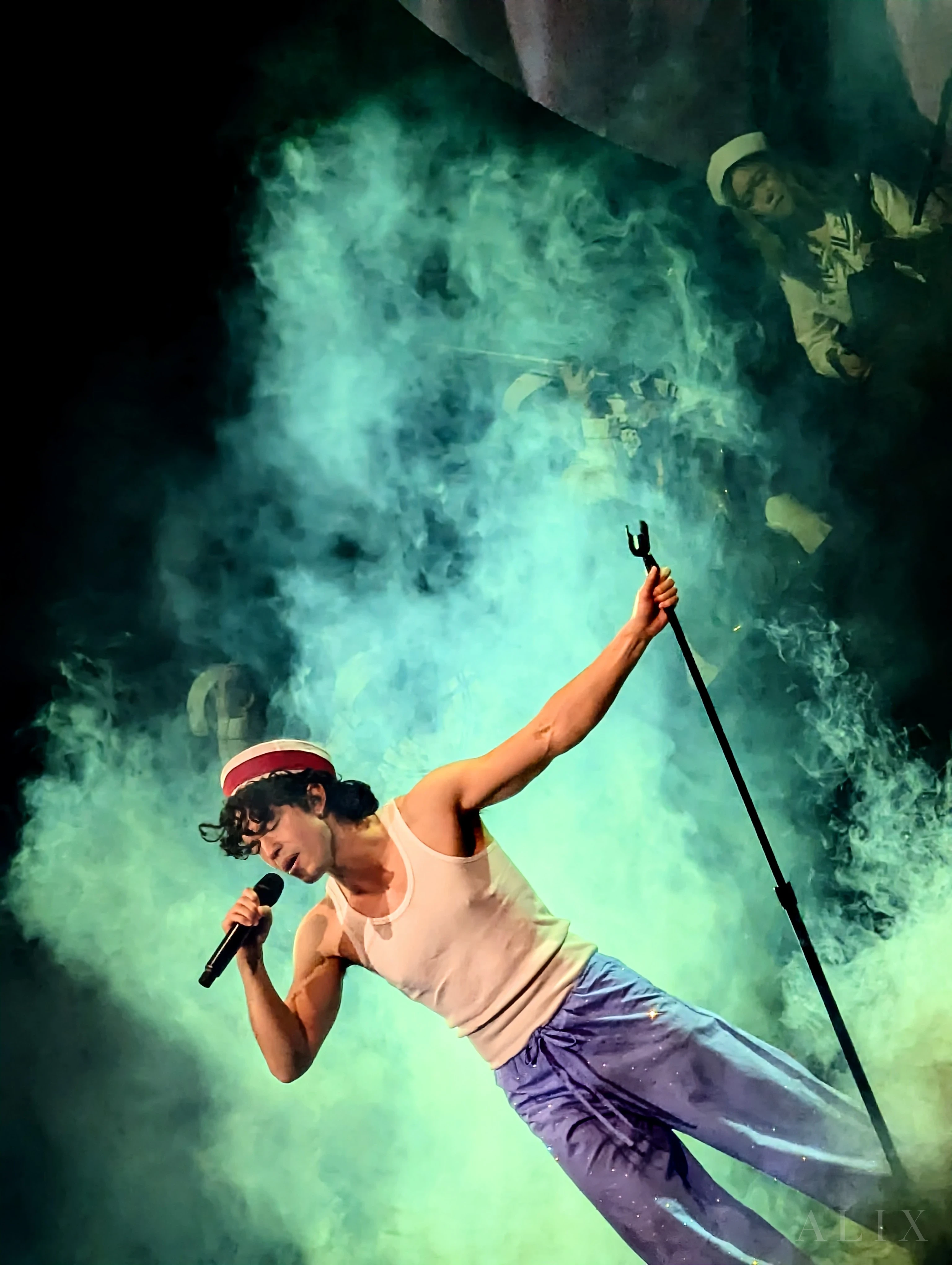 Conan Gray leans into a microphone amid green stage smoke.