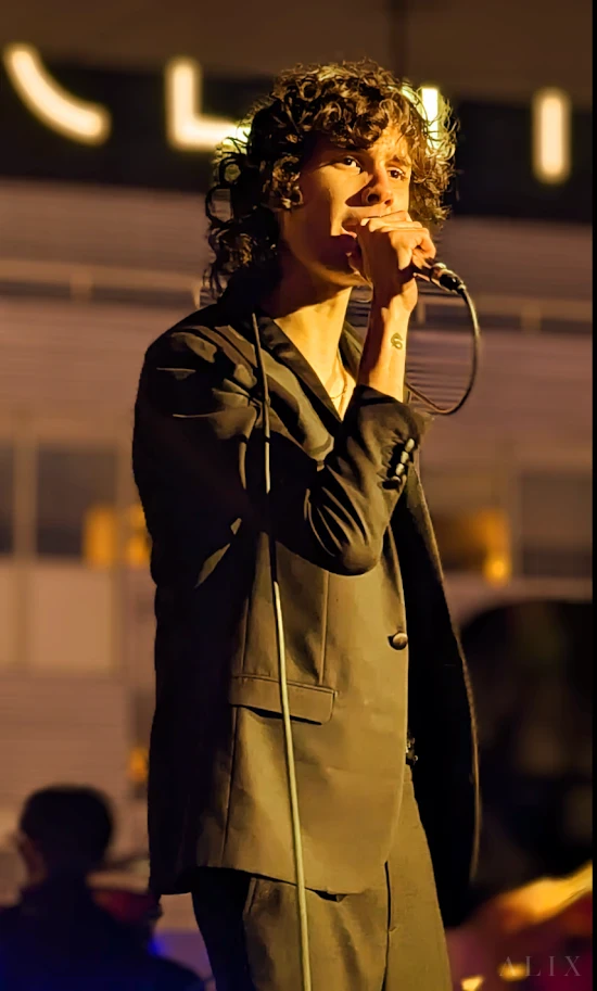 A vocalist performing into a microphone under warm amber concert lighting.