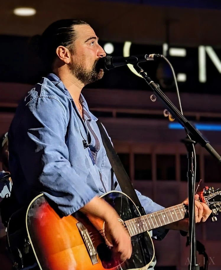 A vocalist leaning toward a microphone on a softly lit stage.