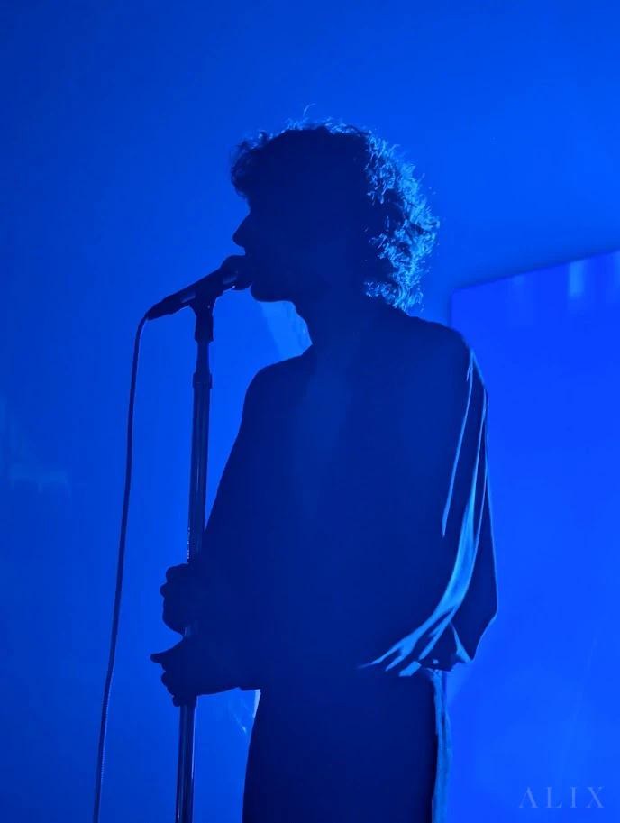 A vocalist silhouetted in deep blue stage lighting.